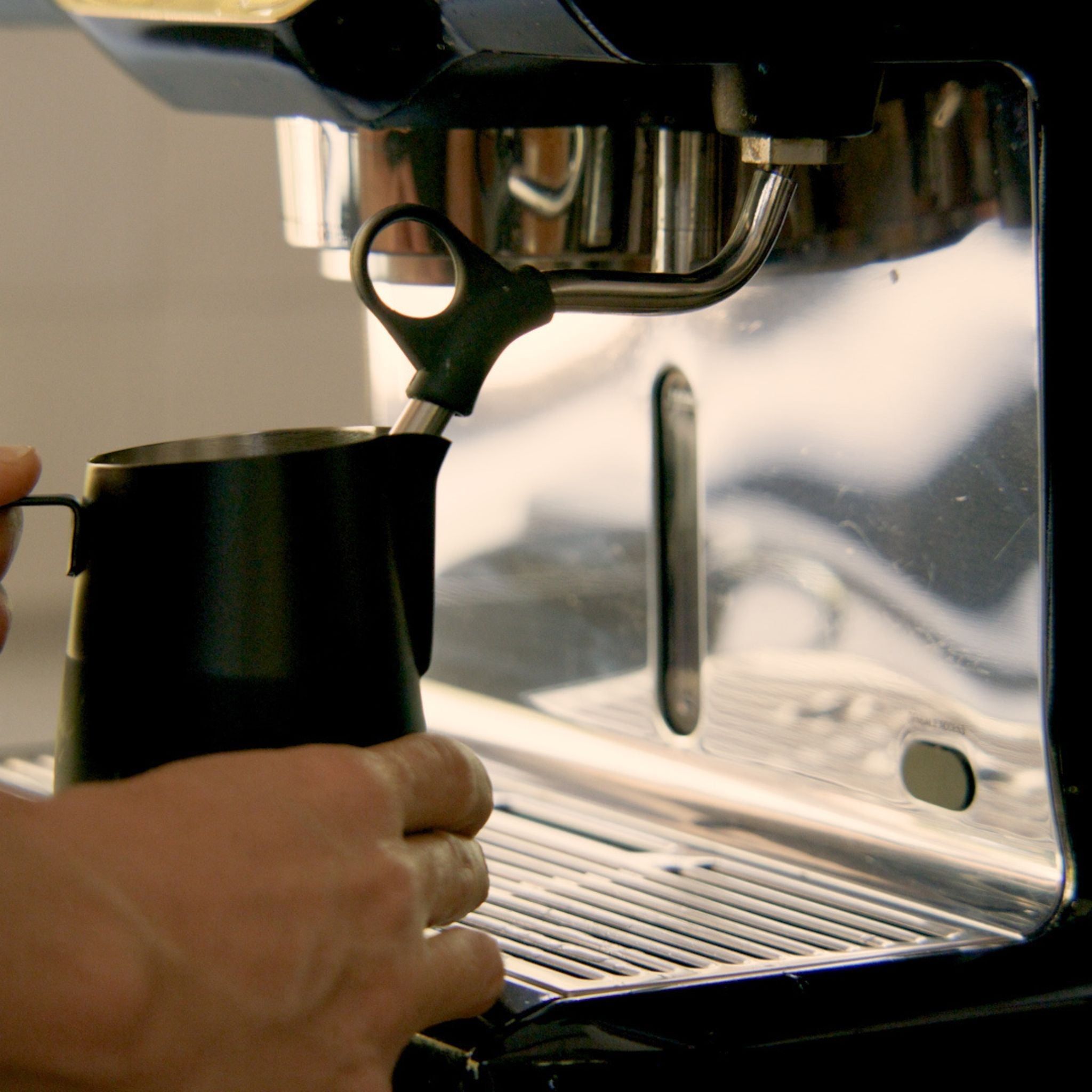 Barista steaming milk in a stainless steel jug under an espresso steam wand